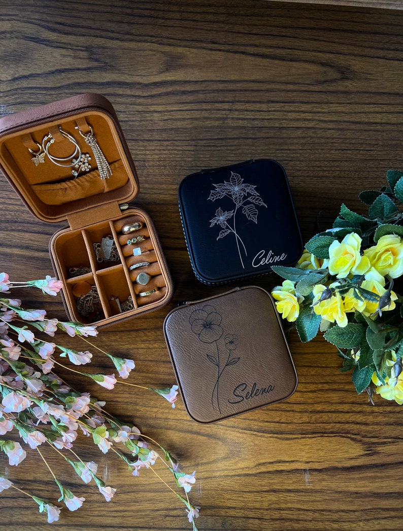 May include: Two brown faux leather jewellery boxes with floral designs and personalised names. The box on the left is open and shows compartments for rings, earrings, and necklaces. The box on the right has the name "Selena" engraved on it. The box in the middle has the name "Celine" engraved on it.