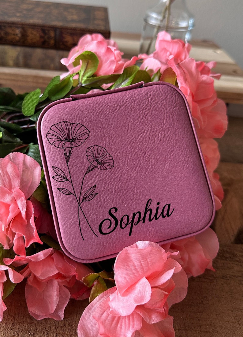 May include: A pink faux leather jewellery box with a floral design and the name "Sophia" engraved on the front.