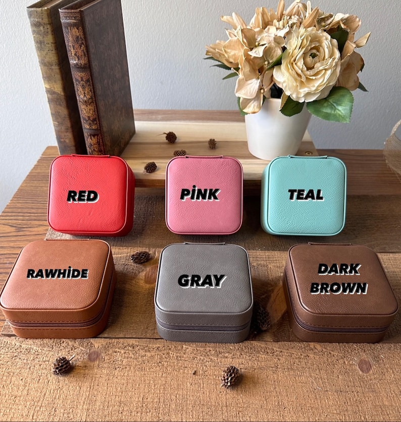 May include: Six small square jewellery boxes in different colours. The boxes are labelled with the colours: Red, Pink, Teal, Rawhide, Grey, and Dark Brown.