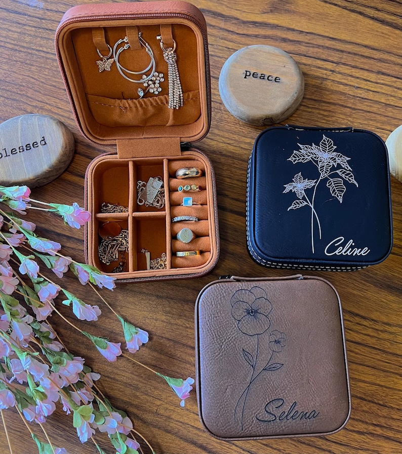 May include: Three brown leather jewellery boxes with different floral designs and personalised names. The boxes are on a wooden surface. The names on the boxes are "Peace", "Celine", and "Selena".