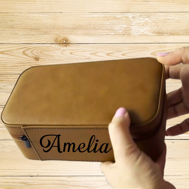 Op de afbeelding: Een bruine leren juwelendoos met een ritssluiting en de naam "Amelia" gegraveerd op de voorkant.