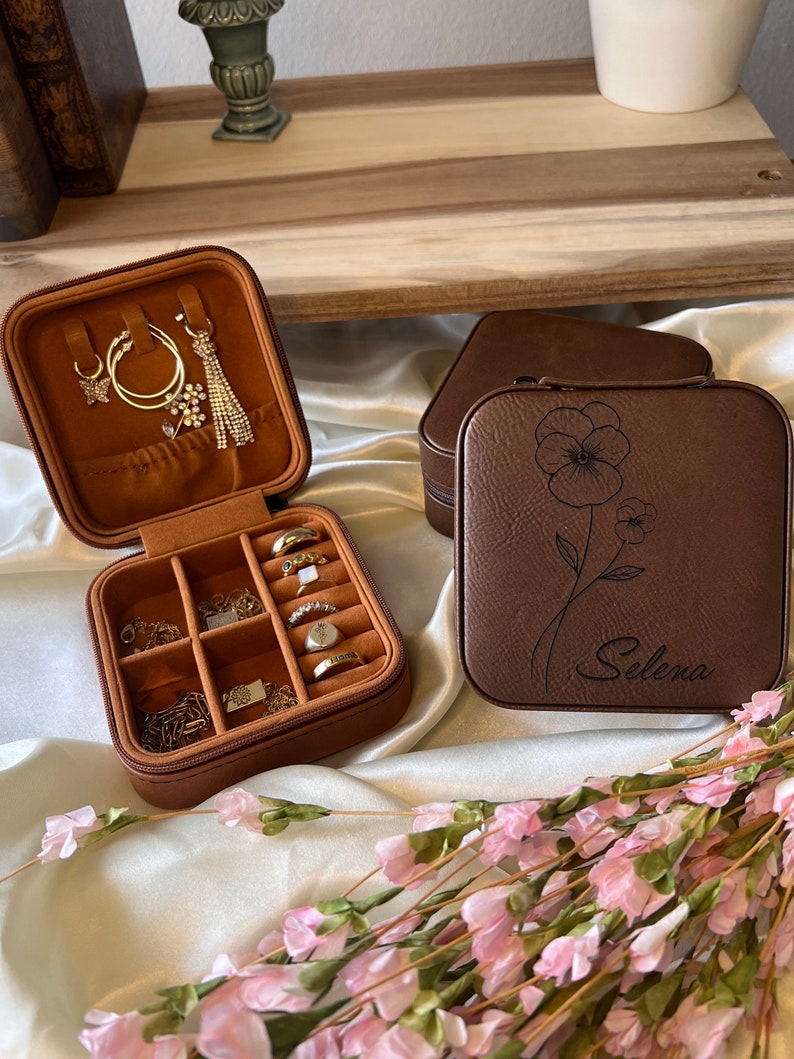May include: Two brown faux leather jewellery boxes. One box has compartments for rings and earrings. The other box has a floral design and the name "Selena" engraved on the front.