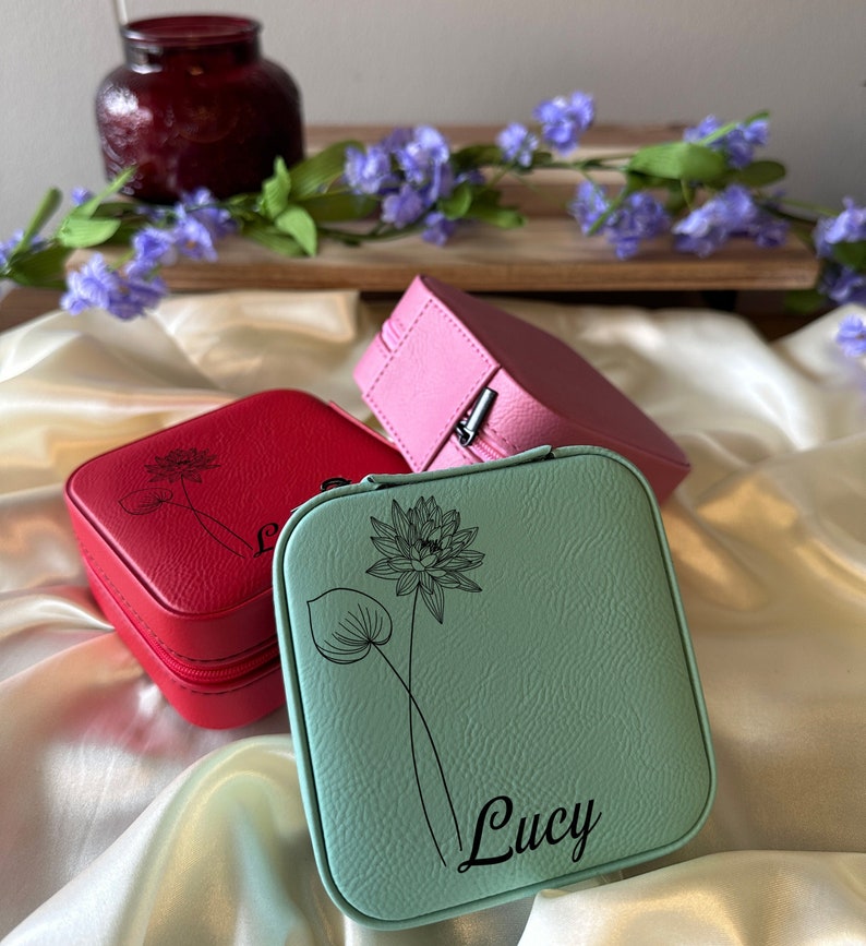 May include: Three small square jewellery boxes with zips. The boxes are red, pink and light blue. The light blue box has a floral design and the name "Lucy" engraved on it.