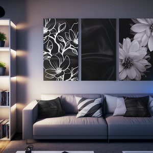 May include: A modern living room featuring a gray sofa with decorative pillows and three black and white floral wall art pieces. A white bookshelf with plants and books is on the left. The room is illuminated by soft lighting.