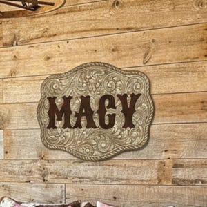 May include: A rustic bedroom scene featuring a wooden wall and a decorative metal sign that reads "MAGY". The bed has pink paisley pillows and a cowhide patterned pillow. A wagon wheel chandelier hangs above the bed.