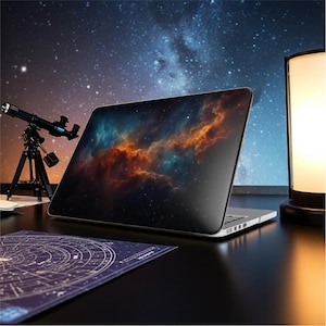 Può includere: Un laptop argentato mostra un vivace design di nebulosa sullo schermo, con tonalità arancioni e verde acqua su uno sfondo scuro. Un piccolo telescopio e una carta stellare sono nelle vicinanze.