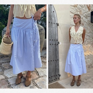 Puede incluir: Falda envolvente a rayas azules y blancas con dobladillo con volantes. La falda se combina con un top color crema y sandalias marrones. En una imagen se sostiene una cesta de paja. La falda es hasta la rodilla.
