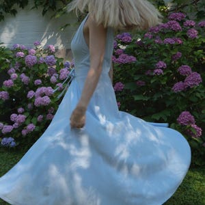 May include: A light blue sleeveless wrap dress with a V-neckline and a tie waist. The dress features a full, flared skirt that is captured in motion, creating a wide, circular silhouette that extends outward from the waistline.
