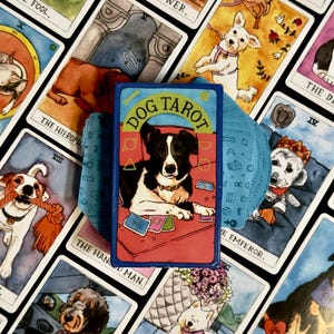 Può includere: Un mazzo di carte dei Tarocchi dei Cani con un cane bianco e nero sulla copertina. Le carte presentano illustrazioni di cani a tema tarocchi. Il mazzo è circondato da altre carte con diverse illustrazioni di cani.