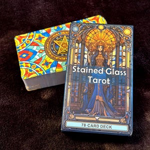 Può includere: Due mazzi di carte dei tarocchi. Uno presenta un colorato design a vetrata con una stella. L'altro mazzo è etichettato "Stained Glass Tarot" e raffigura una donna in abito blu. Il mazzo è etichettato "78-CARD DECK".