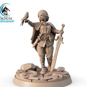 May include: A miniature figurine of a female character with short blonde hair, wearing a brown tunic and a cloak, holding a sword in one hand and a small bird in the other. The figurine is standing on a circular base with a textured surface.