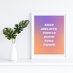 May include: A white framed print with a gradient background of purple, pink, and orange. The text "SIGUE ADELANTE, TODO LO BUENO TOMA TIEMPO" is written in white with a blue outline.