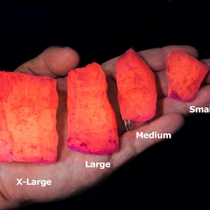 May include: Four pieces of glowing orange rock, labelled X-Large, Large, Medium, and Small. The rocks have a textured surface and a vibrant, neon-like colour. The image is set against a black background.