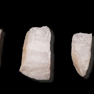 Op de afbeelding: Vier ruwe, lichtroze kwartskristallen van verschillende grootte zijn geplaatst tegen een zwarte achtergrond. De kristallen hebben ruwe, natuurlijke randen en een doorschijnend uiterlijk, dat hun minerale structuur laat zien. De belichting benadrukt de subtiele kleurvariaties.