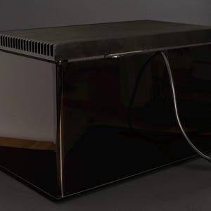 May include: A black rectangular box with a black cord attached to it. The box has a vent on the top and a glossy finish.