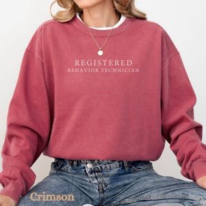 Pode incluir: Uma camisa de moletom vinho com o texto "REGISTERED BEHAVIOR TECHNICIAN" impresso em branco.