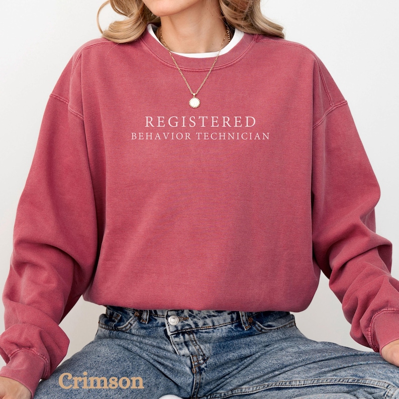 Pode incluir: Uma camisa de moletom vinho com o texto "REGISTERED BEHAVIOR TECHNICIAN" impresso em branco.