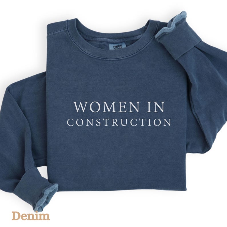 Op de afbeelding: Een donkerblauw sweatshirt met de tekst "WOMEN IN CONSTRUCTION" in wit gedrukt op de voorkant.