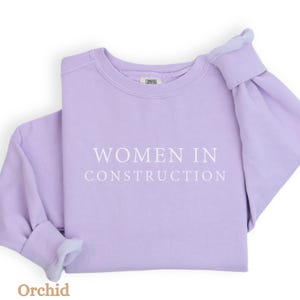 Op de afbeelding: Een lavendelkleurig sweatshirt met de tekst "Women in Construction" in wit gedrukt op de voorkant.
