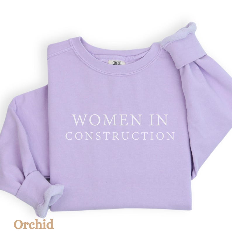 Op de afbeelding: Een lavendelkleurig sweatshirt met de tekst "Women in Construction" in wit gedrukt op de voorkant.