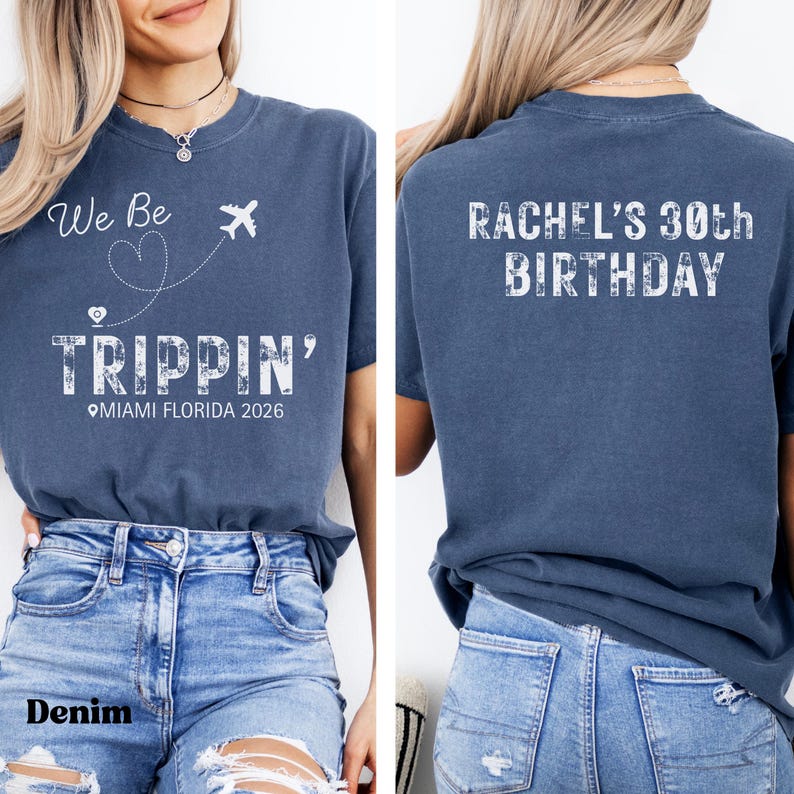 May include: Denim blue t-shirt with white text and graphics. The front of the shirt says "We Be Trippin'" with a heart, airplane, and the location "Miami Florida 2026." The back says "Rachel's 30th Birthday."