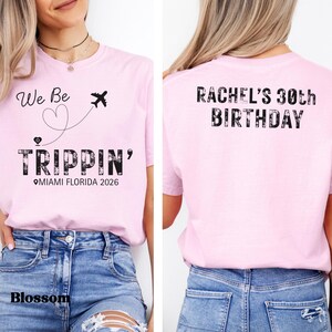 May include: A light pink t-shirt with the text "We Be Trippin'" and a graphic of an airplane and heart. The text "Miami Florida 2026" is also printed on the front. The back of the shirt says "Rachel's 30th Birthday".
