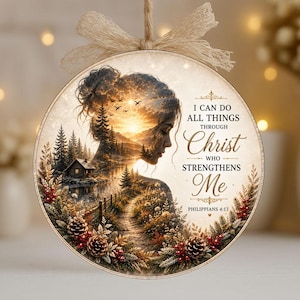 Pode incluir: Um ornamento redondo suspenso com a silhueta de perfil de uma pessoa preenchida por uma paisagem de pôr do sol com pinheiros, uma cabana e pássaros. O texto diz I CAN DO ALL THINGS THROUGH Christ WHO STRENGTHENS Me PHILIPPIANS 4:13, com pinhas.