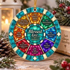 Può includere: Un ornamento circolare con un design a vetrata e un medaglione centrale color verde acqua con la scritta Blessed Are... Matthew 5. I segmenti circostanti mostrano le Beatitudini in colori vivaci come giallo, rosso e viola.