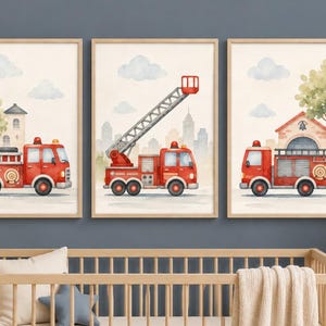 May include: Three framed watercolor prints featuring red fire trucks with varying designs. Each print includes a light beige background with soft clouds and a cityscape or building. The prints are in a nursery setting.