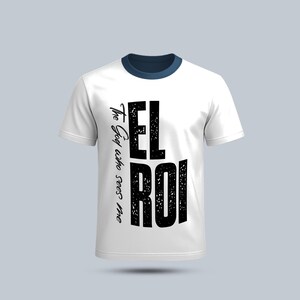 以下が含まれることがあります： ネイビーブルーの襟と、大きな黒い文字で「EL ROI」と書かれた白いTシャツ。「The God who sees me」というフレーズが筆記体で縦書きされています。