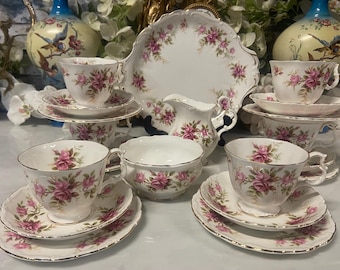 May include: A vintage tea set featuring white porcelain cups, saucers, and a serving plate, all adorned with pink rose floral patterns and gold trim. Includes a creamer and sugar bowl. A classic and elegant design.