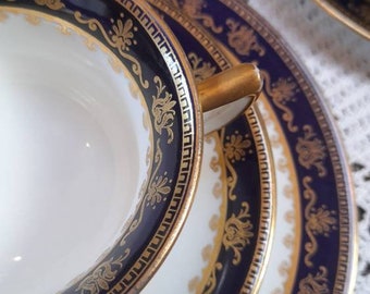 May include: A set of three white porcelain plates with a blue and gold rim. The plates have a decorative pattern of gold flowers and leaves on a blue background.