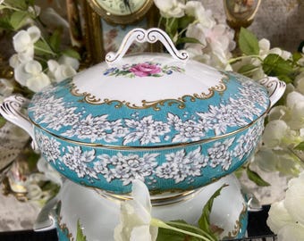 May include: A large, white porcelain serving dish with a teal and gold floral design. The dish has a lid with a gold handle and a floral design.
