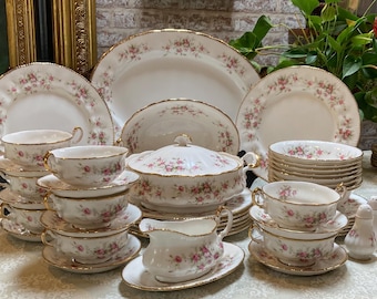 Op de afbeelding: Een set wit porselein serviesgoed met een delicaat bloemenpatroon. De set bevat borden, kommen, kopjes en schoteltjes. De stukken zijn afgewerkt met gouden accenten.