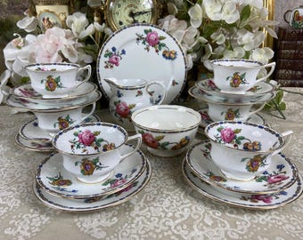Könnte beinhalten: Ein Vintage-Blumenservice mit weißem Hintergrund und goldener Verzierung. Das Set beinhaltet eine Teekanne, eine Zuckerdose, eine Milchkännchen, Tassen und Untertassen. Das Blumenmuster zeigt rosa, gelbe und blaue Blumen.