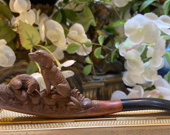 May include: A wooden pipe with a carved design of a dog and a badger. The pipe is brown and has a black mouthpiece.