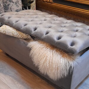 May include: A gray tufted storage ottoman with a plush velvet top and a soft, fluffy white faux fur lining the inside. The ottoman is open and the lid is propped up.