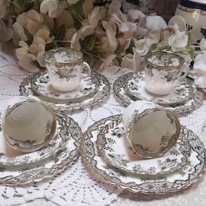 Op de afbeelding: Set van vier vintage theekopjes en schoteltjes met een groen en gouden bloemenpatroon. De kopjes en schoteltjes hebben een gegolfde rand.