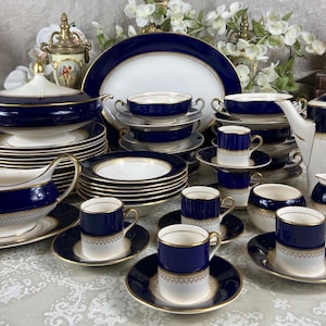 Puede incluir: Un juego de vajilla de porcelana azul y blanca con detalles dorados. El juego incluye platos, cuencos, tazas, platillos, una salsera, una tetera y un azucarero.