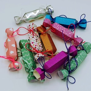 Könnte beinhalten: Eine Sammlung bunter, festlicher Papier-Süßigkeitenboxen mit verschiedenen Mustern und Designs. Die Boxen sind mit Bändern gebunden und bereit, mit Leckereien gefüllt zu werden.