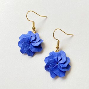 Könnte beinhalten: Ein Paar handgefertigte blaue Origami-Blumenohrringe mit goldfarbenen Ohrhaken. Die Ohrringe haben ein spiralförmiges Design, wobei jedes Blütenblatt sorgfältig gefaltet ist. Die Ohrringe sind leicht und für den Alltag geeignet.