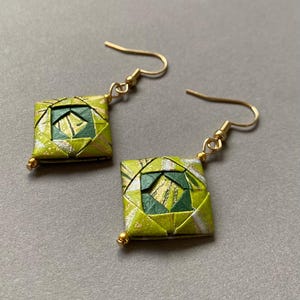 K&ouml;nnte beinhalten: Ein Paar quadratische Origami-Ohrringe mit goldfarbenen Ohrdr&auml;hten und kleinen goldenen Perlen. Die Ohrringe weisen ein geometrisches Design in Gr&uuml;n-, Gold- und Silbert&ouml;nen auf. Die Ohrringe werden auf grauem Hintergrund pr&auml;sentiert.