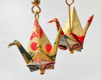 May include: Gold origami crane earrings with red and green patterned paper. The cranes are hanging from gold hooks with gold beads.