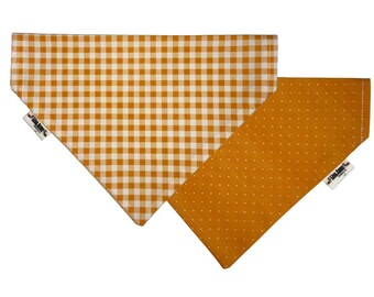 May include: Two dog bandanas. One is a golden yellow and white gingham pattern. The other is a solid golden yellow with small white polka dots. Both bandanas have a triangular shape and are made of fabric.