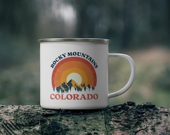 May include: White enamel camping mug with a retro design featuring a sunset over mountains and the text "Rocky Mountains Colorado".