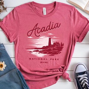 May include: A red t-shirt with a graphic of a lighthouse and the text "Acadia National Park Maine".
