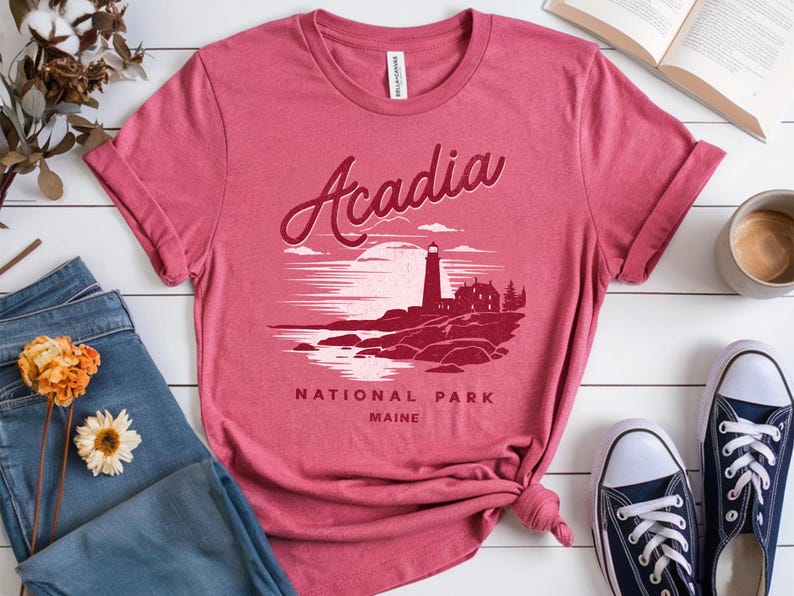 May include: A red t-shirt with a graphic of a lighthouse and the text "Acadia National Park Maine".