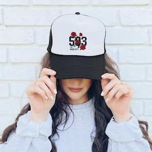 Può includere: Cappellino da camionista bianco e nero con pannello frontale bianco. Il cappello presenta il numero "503" in nero con rose rosse e la scritta "The Rose City" sotto. Il cappello è indossato da una persona.