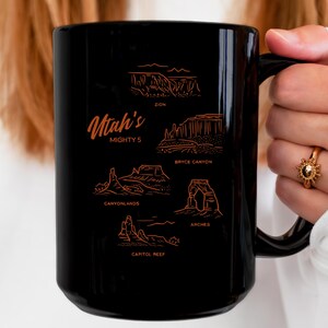 May include: Black ceramic mug with a white outline of the Utah Mighty 5 National Parks: Zion, Bryce Canyon, Canyonlands, Arches, and Capitol Reef. The mug has a white handle.