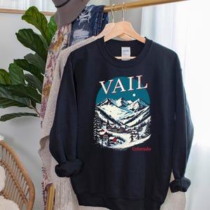 May include: Black sweatshirt with a colorful graphic of a snowy mountain scene and the text "Vail, Colorado".